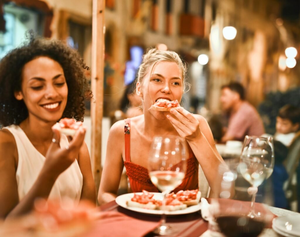 Restoranda iki kadın arkadaş yemek yerken ve şarap içerken gülüyor